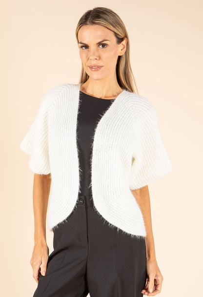 Woman wearing a white knit cardigan over a black top and pants on a beige background