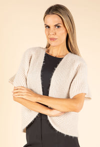 Woman wearing a beige knit cardigan over a black top on a beige background