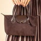 Brown suede handbag held by a person wearing a brown dress with vertical stripes.