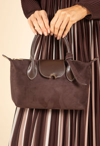 Brown suede handbag held by a person wearing a brown dress with vertical stripes.