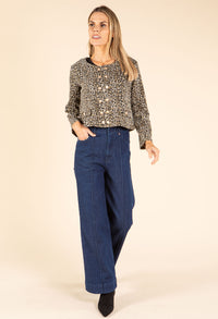 Woman wearing a patterned blouse and blue jeans on a beige background