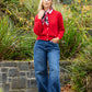 Woman in a red cardigan and blue jeans standing in a garden.
