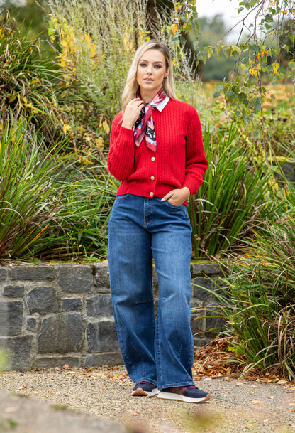 Woman in a red cardigan and blue jeans standing in a garden.