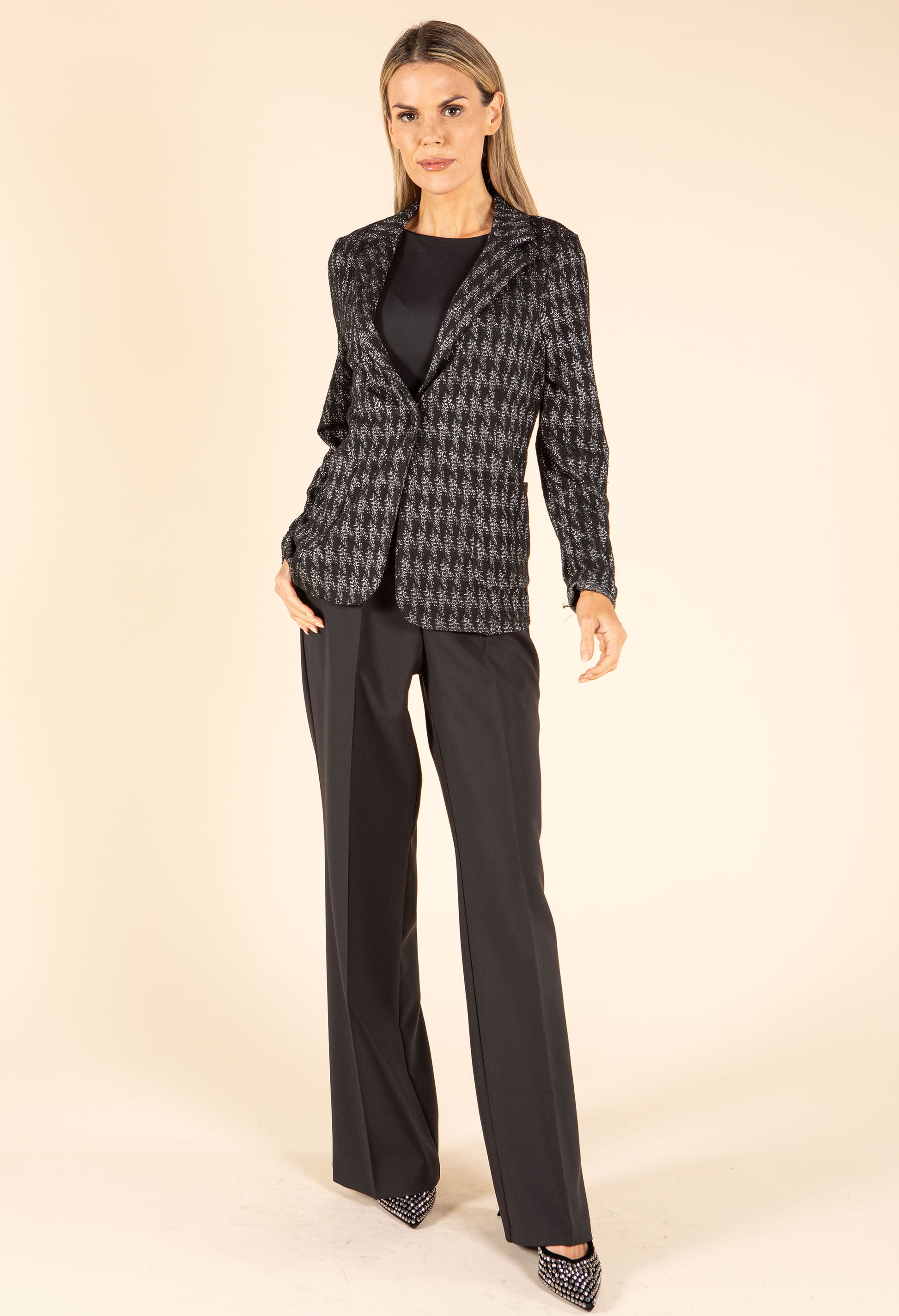 Woman wearing a houndstooth patterned blazer and black pants on a beige background