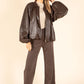 Woman wearing a brown leather jacket and pants on a beige background