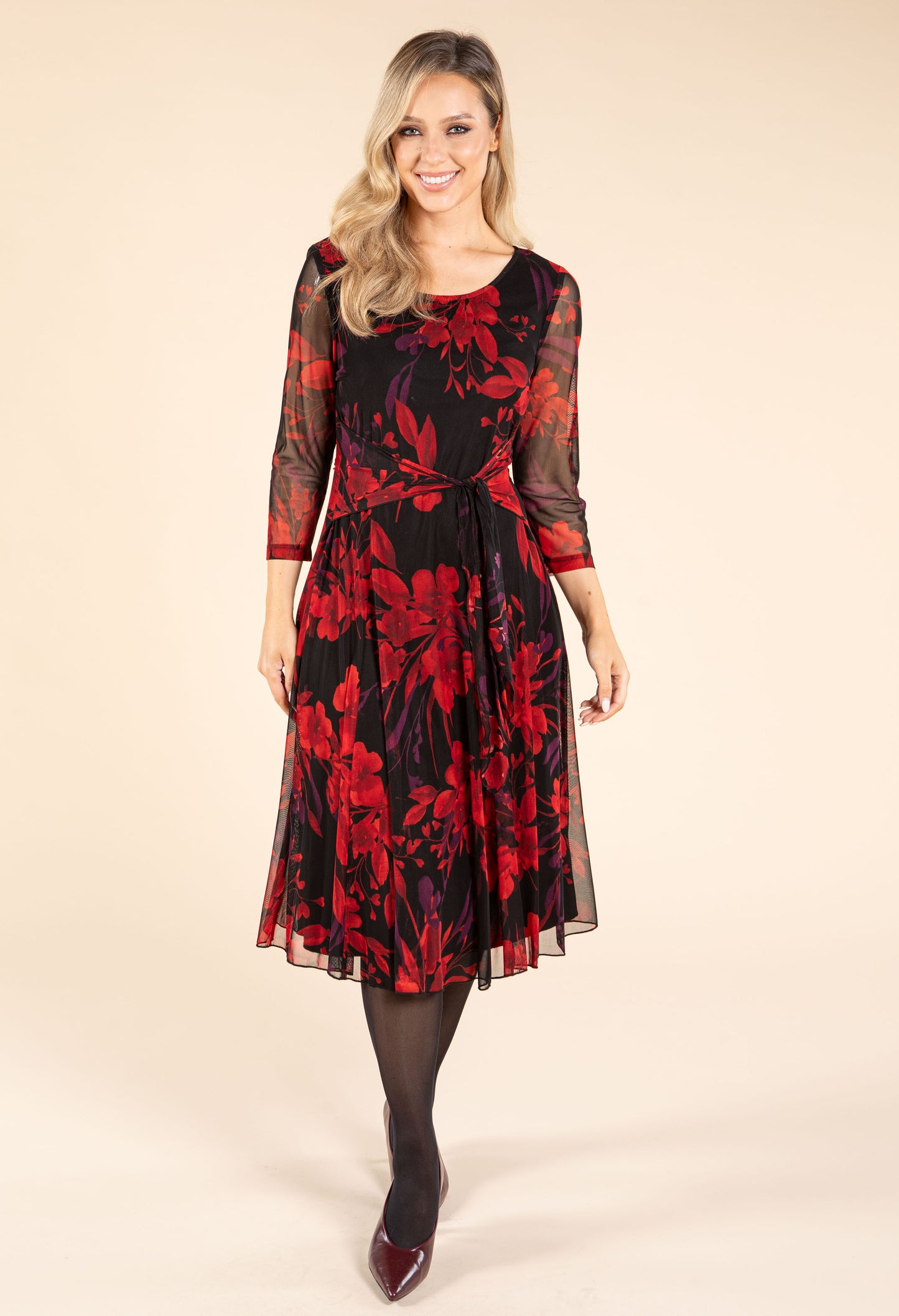 Woman wearing a black dress with red floral pattern on a beige background