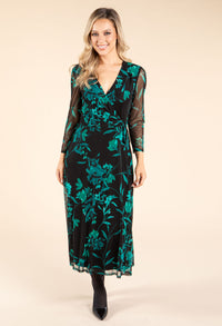 Woman wearing a black dress with green floral pattern on a beige background