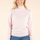 Woman wearing a light pink turtleneck sweater and blue jeans on a beige background