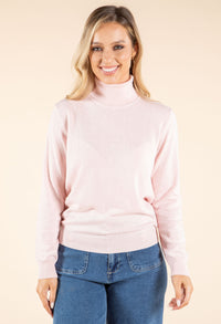 Woman wearing a light pink turtleneck sweater and blue jeans on a beige background