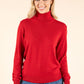 Woman wearing a red turtleneck sweater and blue jeans on a beige background