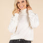 Woman wearing a white turtleneck sweater and dark jeans on a beige background