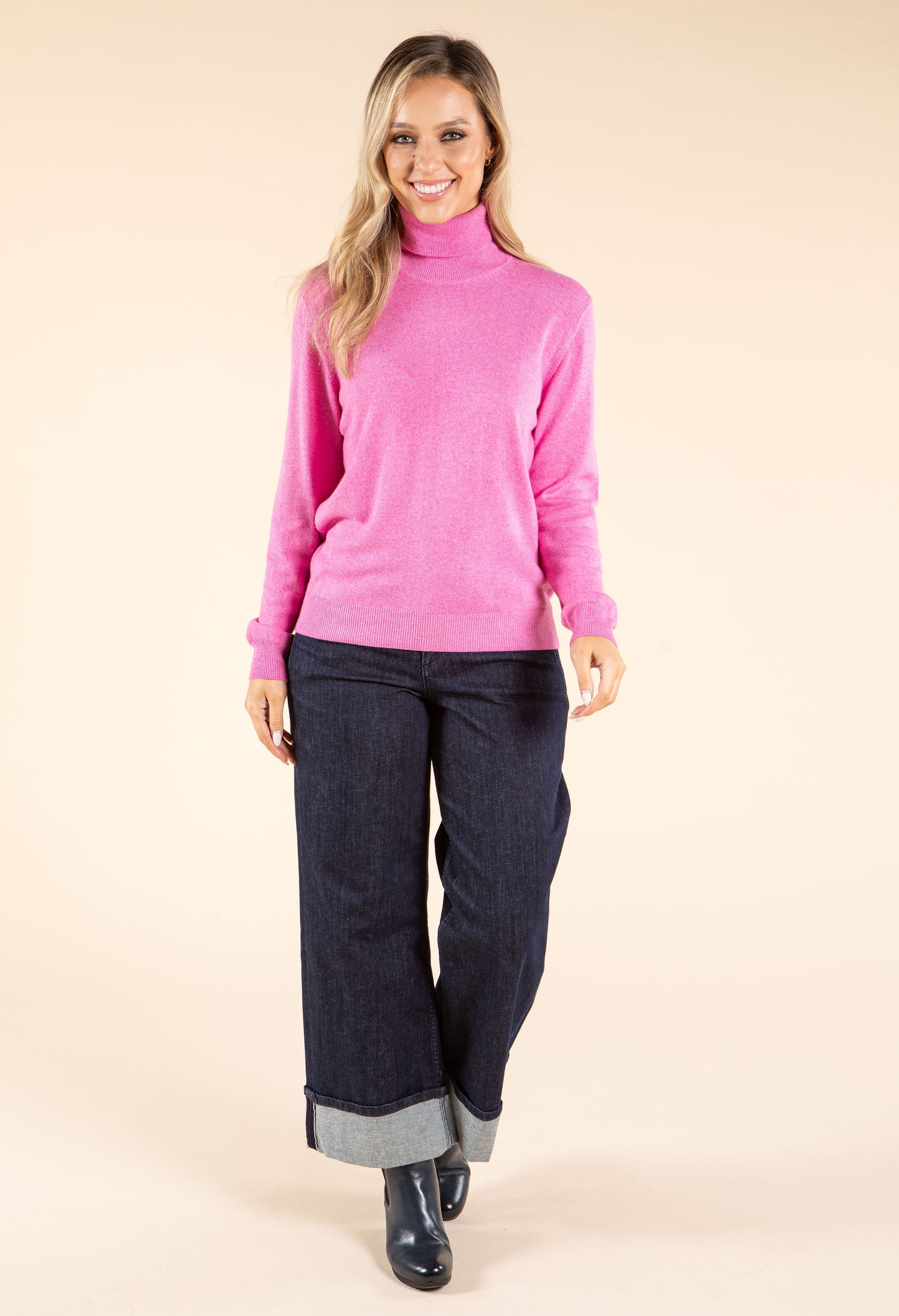 Woman wearing a pink sweater and dark jeans on a beige background