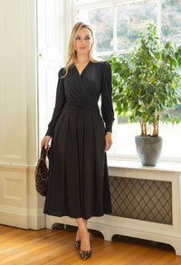 Woman in a black dress standing in a room with a window and plant.