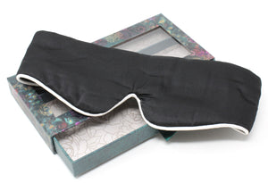 Black sleep mask with white trim on a decorative box