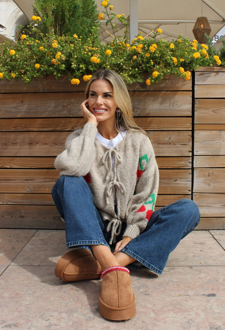 Woman sitting outdoors wearing a cozy outfit with a sweater, jeans, and slippers.