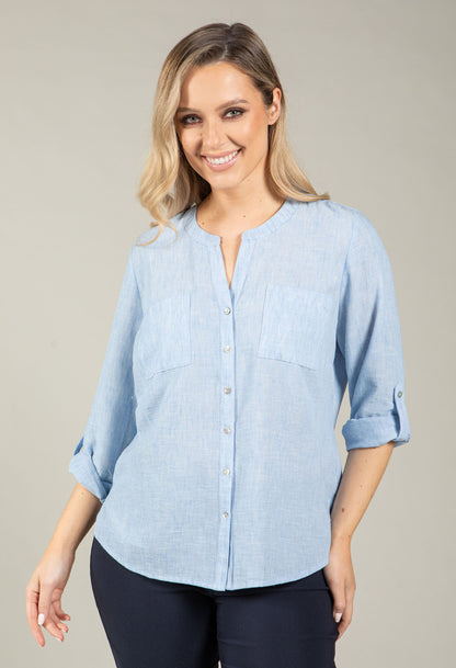 Woman wearing a light blue shirt with rolled-up sleeves against a neutral background