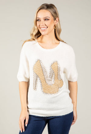 Woman wearing a white sweater with a high-heeled shoe design on a plain background