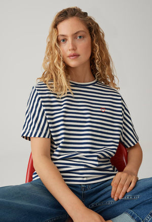 Woman wearing a striped shirt with a small logo, sitting on a red chair against a plain background