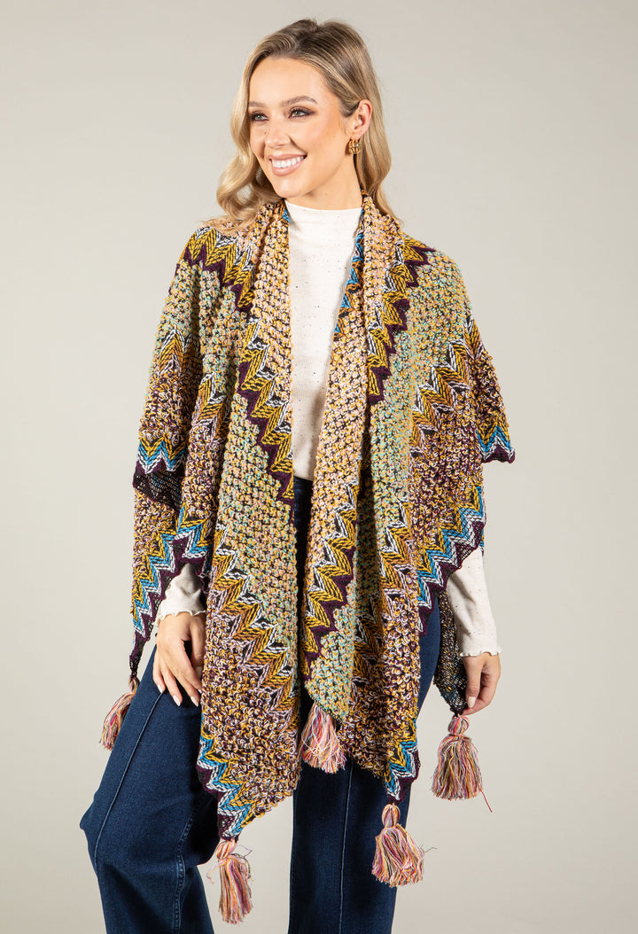 Woman wearing a patterned shawl over a white sweater and jeans on a beige background