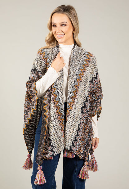 Woman wearing a patterned cardigan with tassels on a plain background