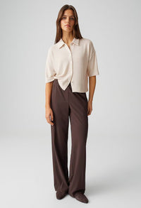 Woman wearing a beige blouse and brown pants on a white background