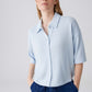 Woman wearing a light blue shirt and dark blue pants against a plain background