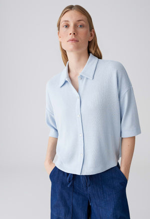 Woman wearing a light blue shirt and dark blue pants against a plain background