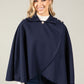 Woman wearing a navy blue cape over a white shirt and jeans on a plain background
