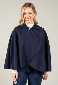 Woman wearing a navy blue cape over a white shirt and jeans on a plain background