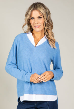 Woman wearing a blue sweater over a white shirt on a plain background