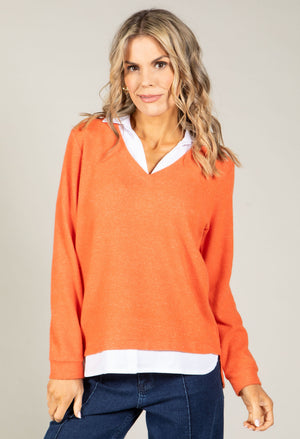 Woman wearing an orange sweater with a white collar against a plain background