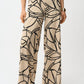 Beige pants with black abstract pattern worn by a person on a white background