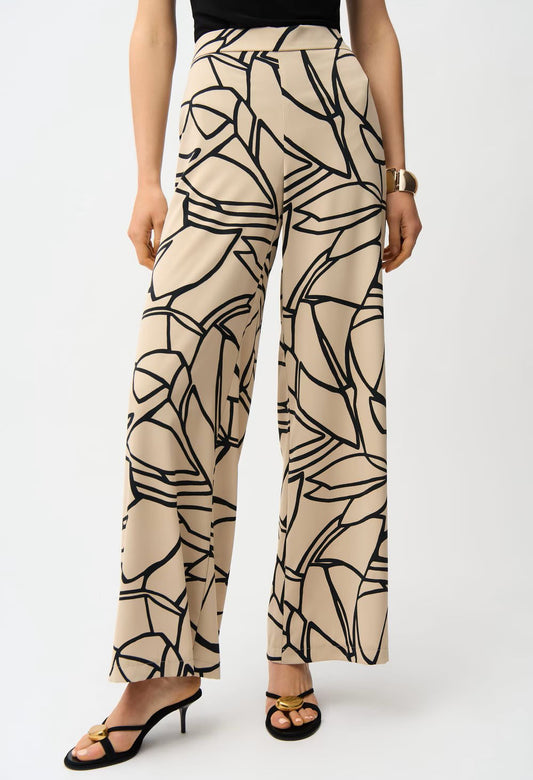 Beige pants with black abstract pattern worn by a person on a white background