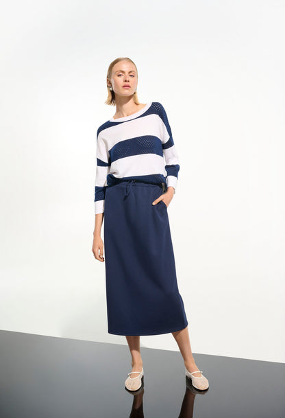 Woman wearing a striped sweater and navy skirt on a white background