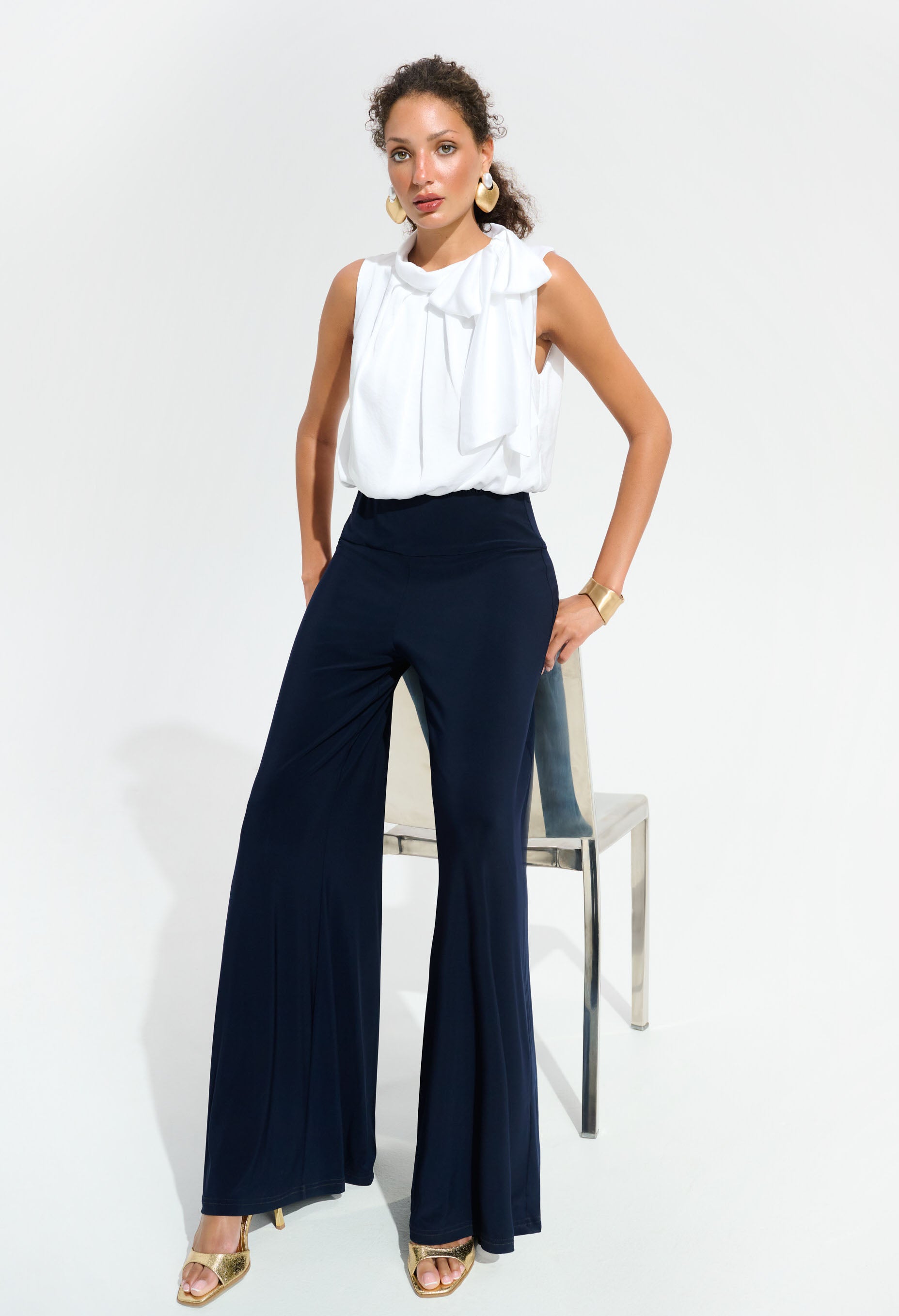 Woman wearing a white blouse and navy pants on a white background