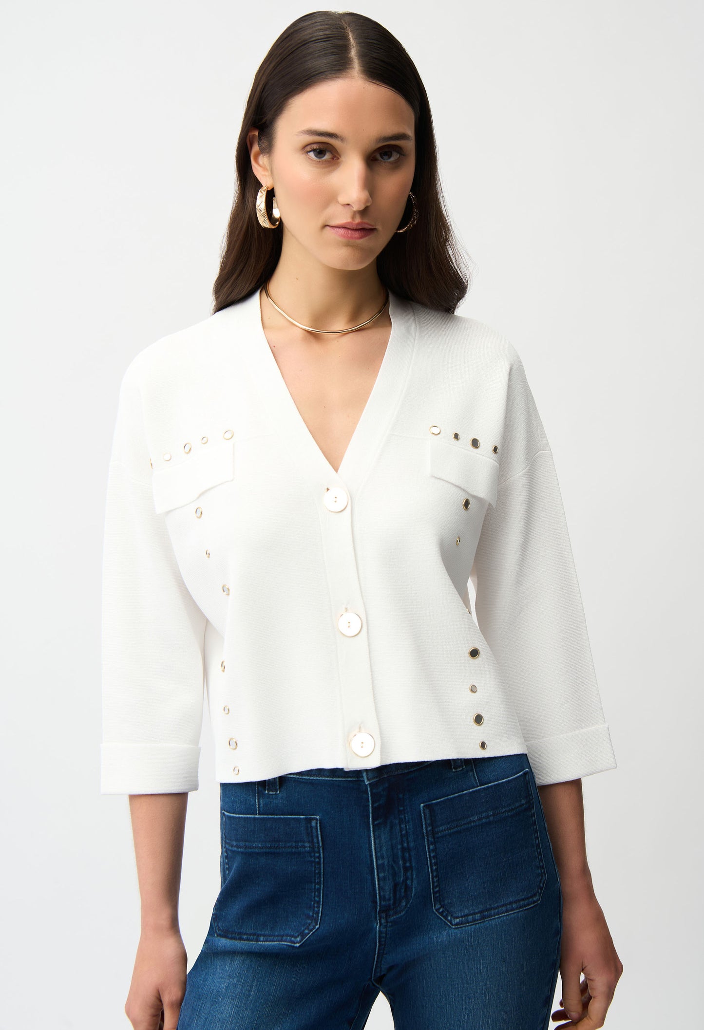 Woman wearing a white blouse with button details and blue jeans on a plain background