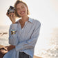 Woman holding a camera by a waterfront wearing a striped blue shirt