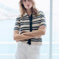 Woman wearing a striped shirt and white pants standing in front of a window with a blurred background