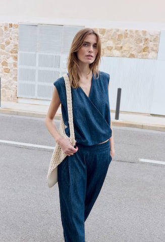 Woman in a blue outfit standing on a street with a stone wall background
