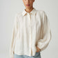 Woman wearing a white button-up shirt and light blue jeans against a plain background