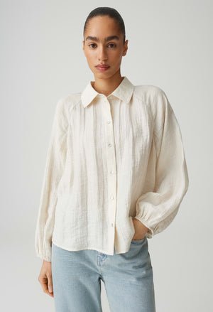 Woman wearing a white button-up shirt and light blue jeans against a plain background