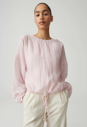 Person wearing a light pink blouse with long sleeves on a plain background