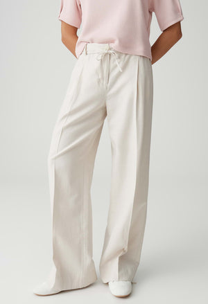 Person wearing light pink top and beige wide-leg pants on a white background