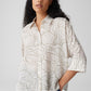 Woman wearing a patterned shirt and blue pants against a plain background