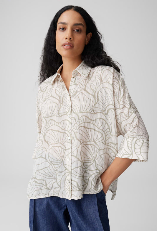 Woman wearing a patterned shirt and blue pants against a plain background