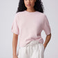 Woman wearing a light pink top and white pants against a plain background
