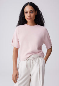 Woman wearing a light pink top and white pants against a plain background