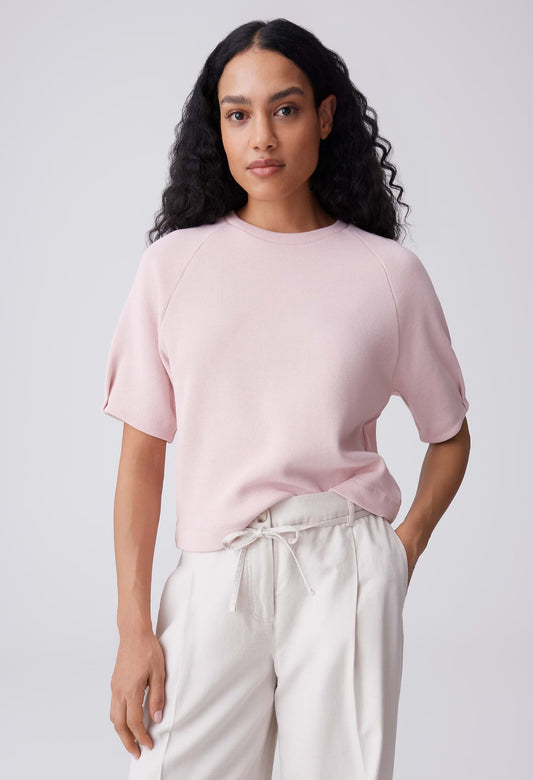 Woman wearing a light pink top and white pants against a plain background