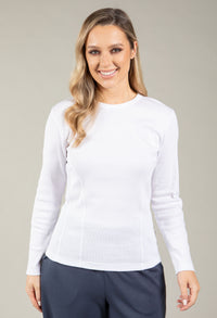 Woman wearing a white long-sleeve top and dark pants against a neutral background