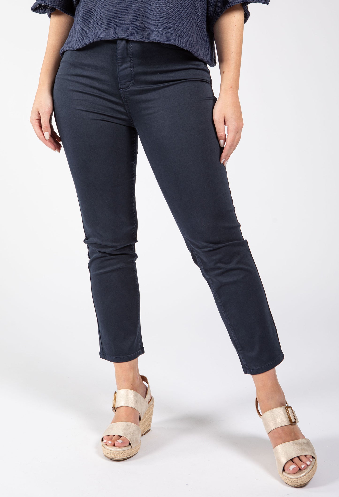 Person wearing navy blue pants and gold sandals on a white background